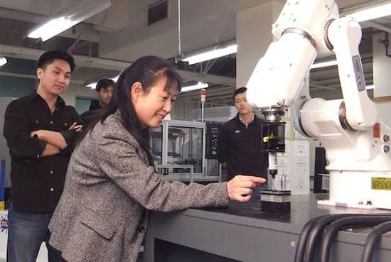 instructor places something at the business end of a robot while students look on